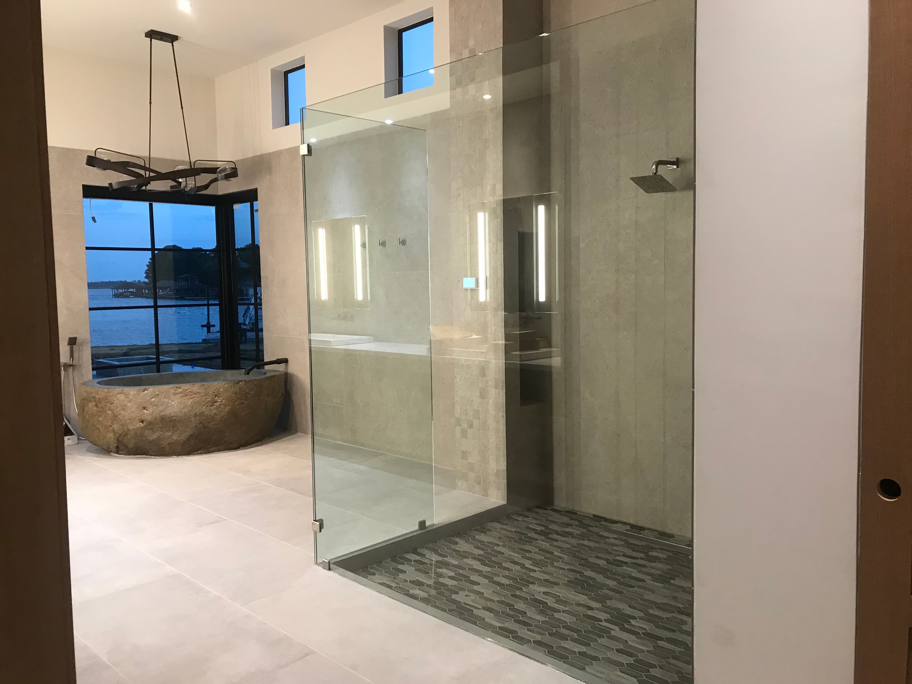 Minimalist bathroom featuring a glass-enclosed shower, carved stone bathtub, and scenic lakefront window views.