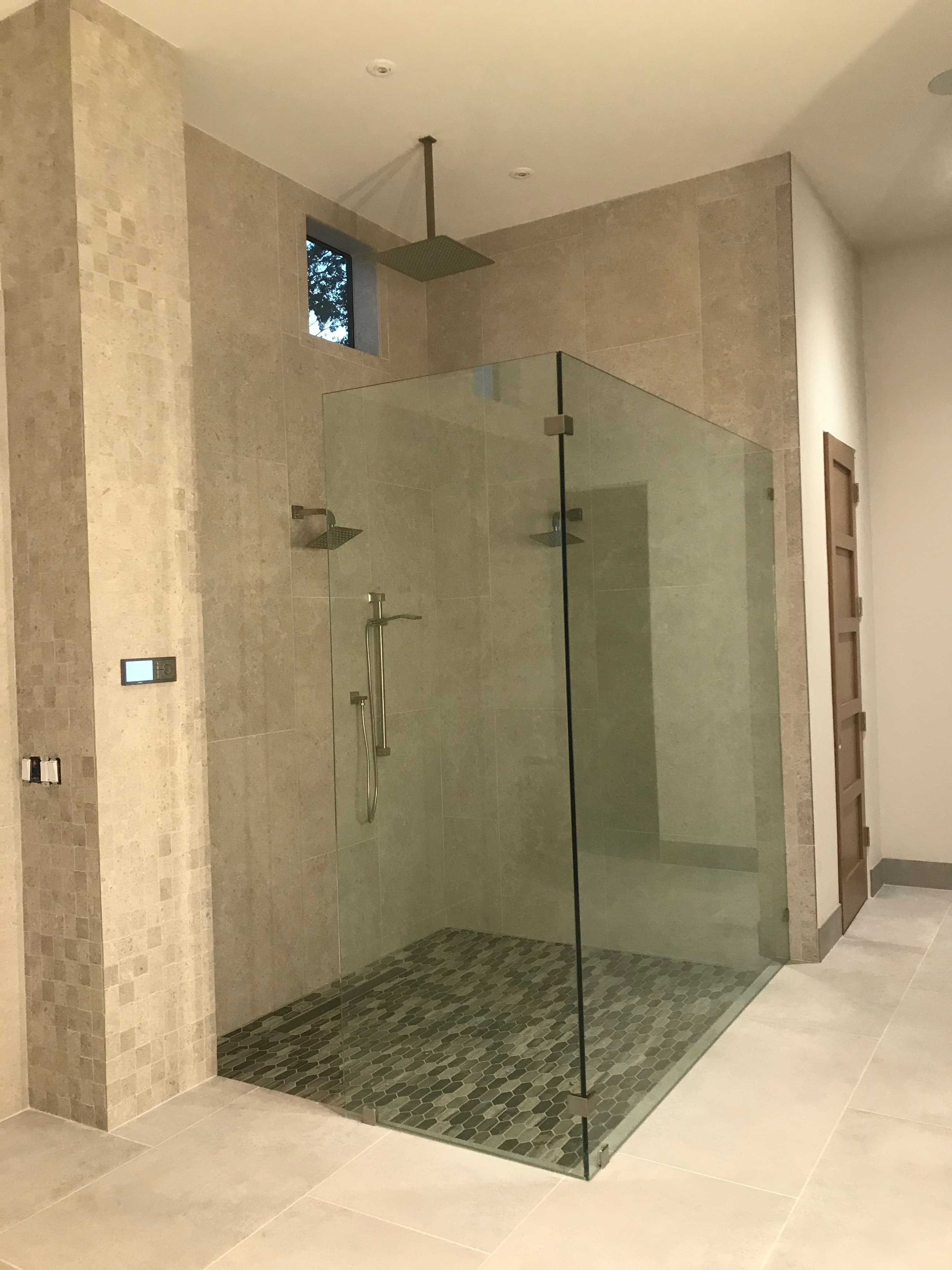 Modern walk-in shower with glass walls, beige stone tiles, and dark hexagonal floor tiles.