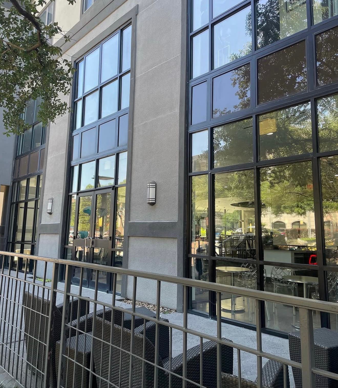 Modern building with large glass windows reflecting trees and a fenced patio with outdoor seating.