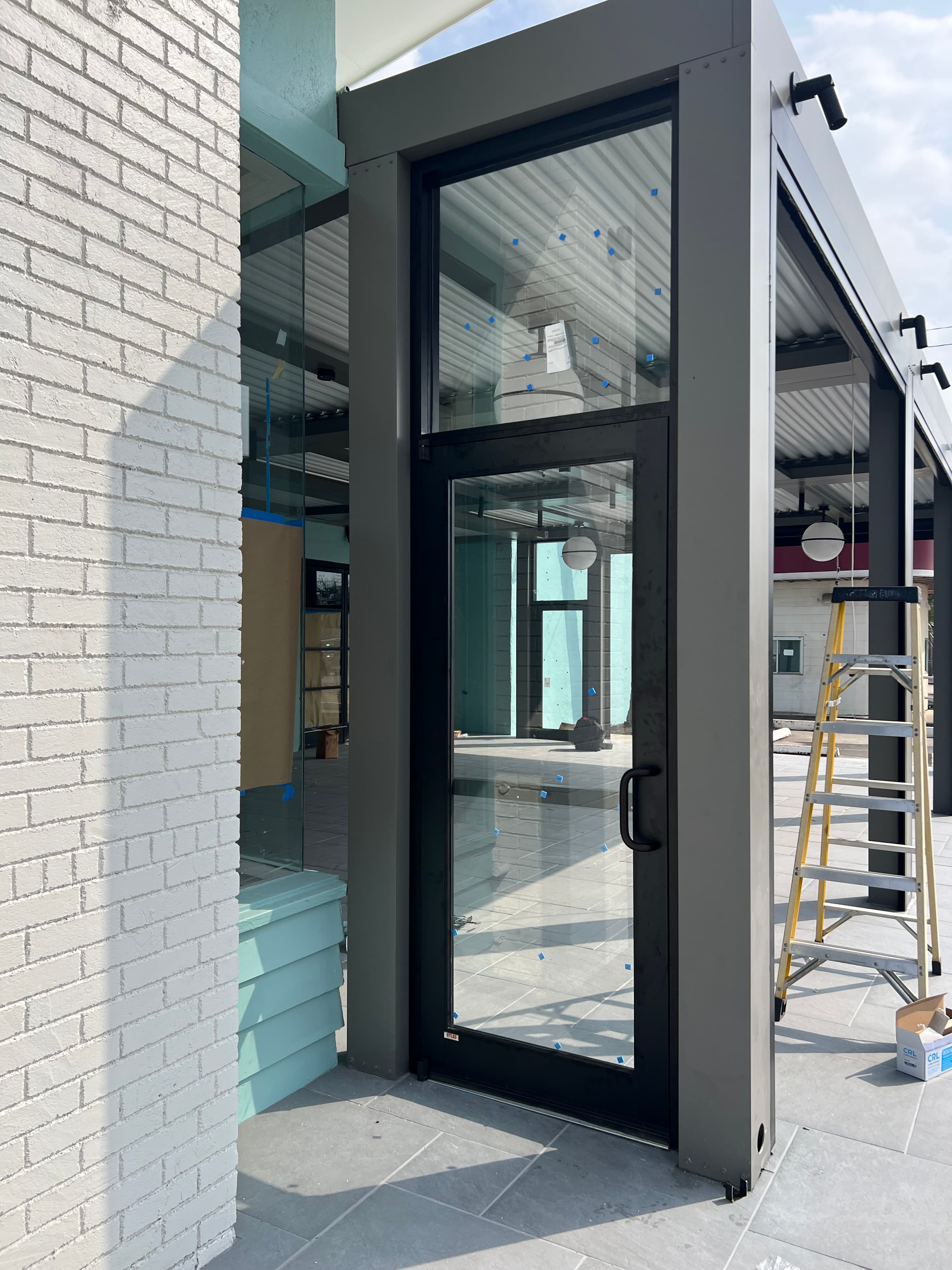 Black-framed glass door installed in a grey metal structure beside a white brick wall.