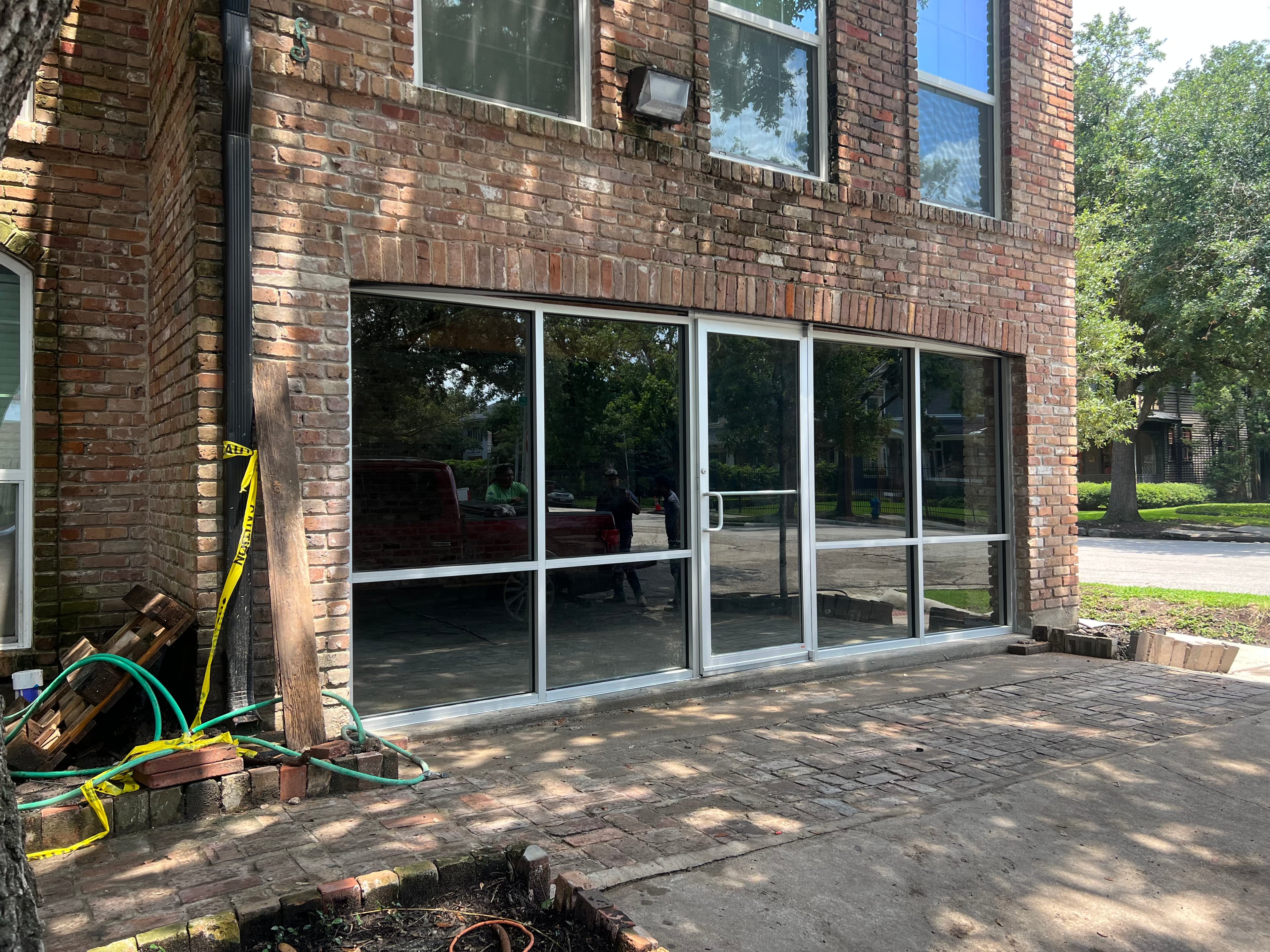 Large glass storefront with silver frames installed in a weathered red brick building exterior.