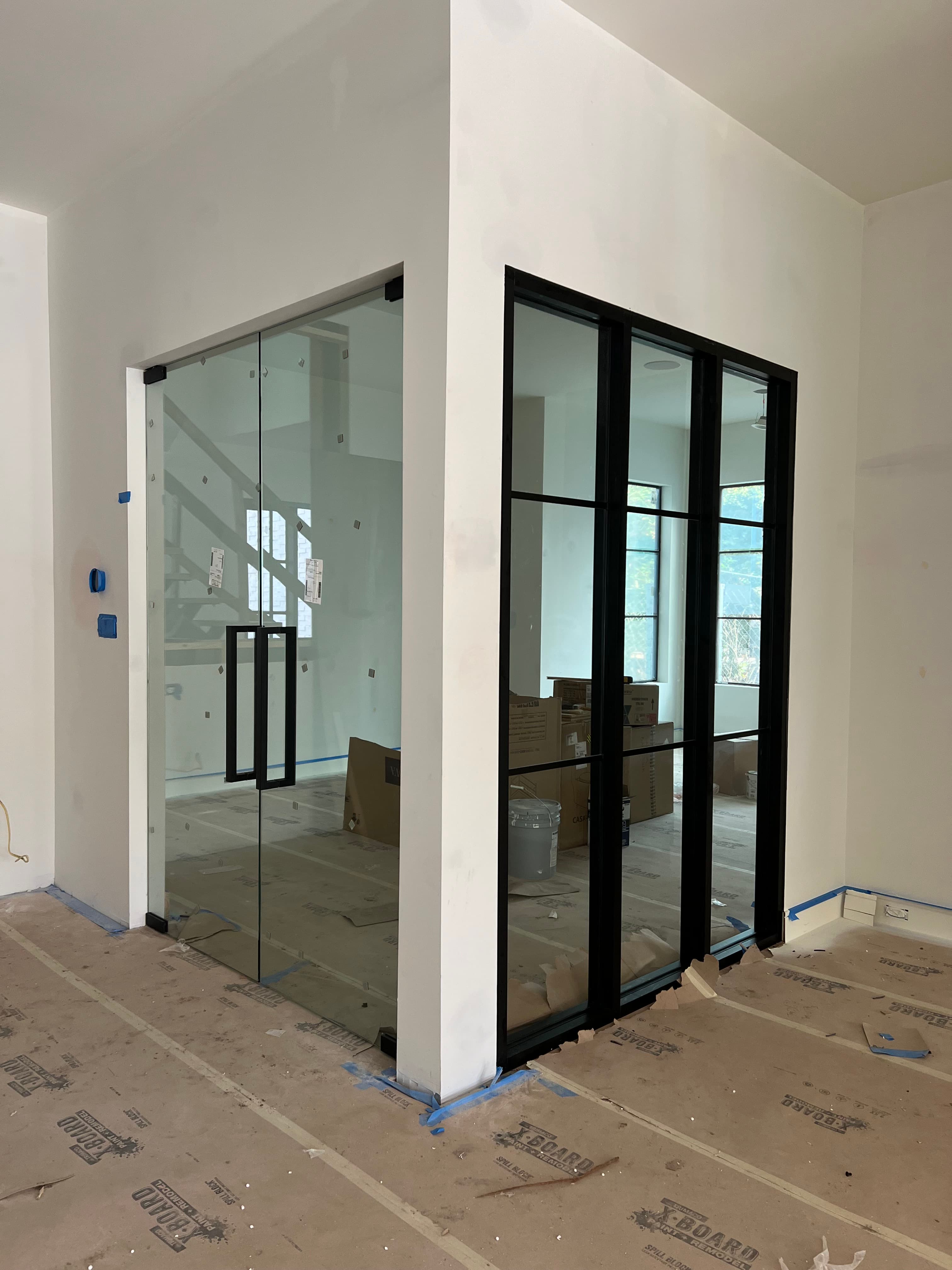 Modern corner glass room with black-framed windows and frameless double doors under construction.